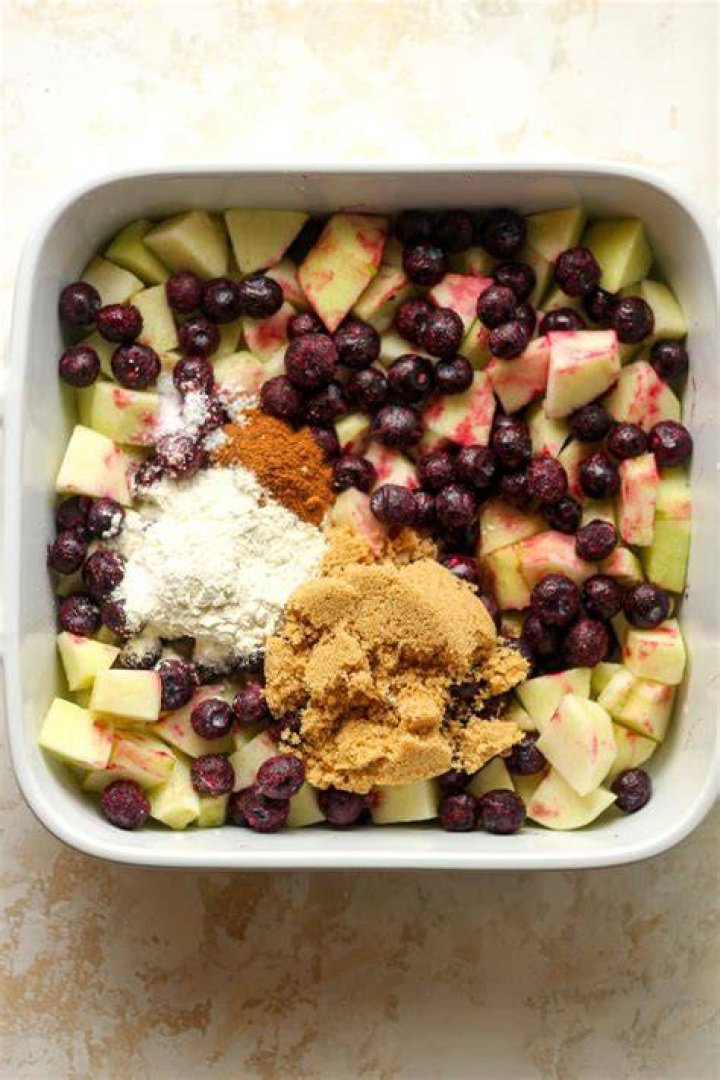 Blueberries with sugar, flour, and lemon zest in a glass bowl.