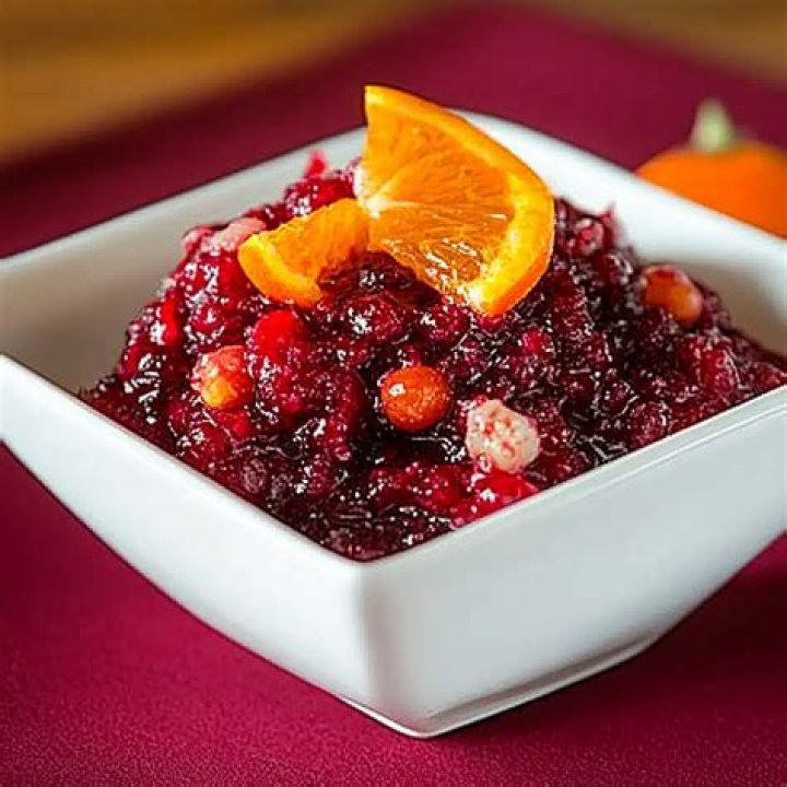 Closeup of cranberry orange relish in a white bowl with a gold spoon.